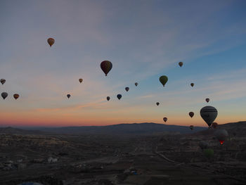 Hot air balloons flying over landscape against sky during sunset