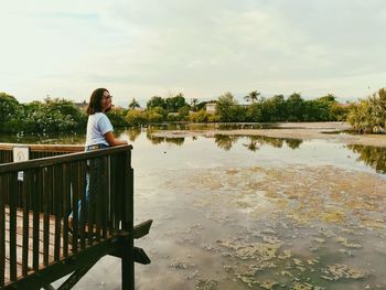 Woman standing on footbridge by lake