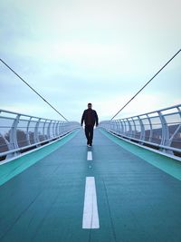 Rear view of man standing on footbridge against sky