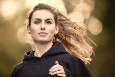 Portrait of young woman with arms raised standing outdoors