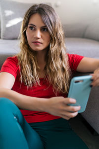 Portrait of beautiful young woman using phone while sitting on sofa
