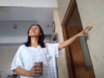 Young woman looking away while standing against wall
