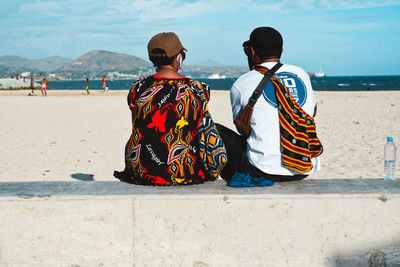 Rear view of people sitting on beach against sky