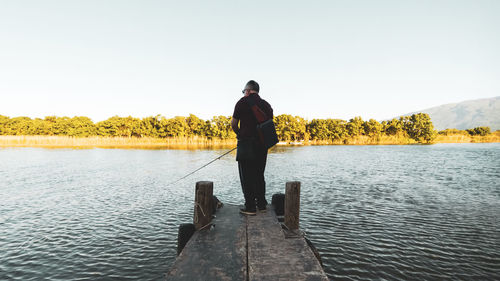 Rear view of man standing in lake against clear sky