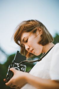 Portrait of teenage girl holding camera against sky