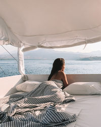 Rear view of woman sitting on bed at beach