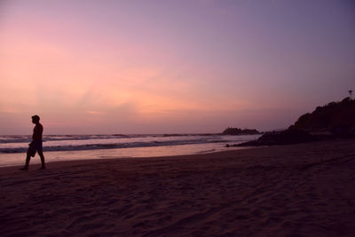 Silhouette mid adult man walking at beach against sky during sunset