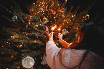 Teenage girl holding sparklers standing by luminous christmas tree