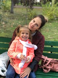 Portrait of smiling girl with mother sitting on bench