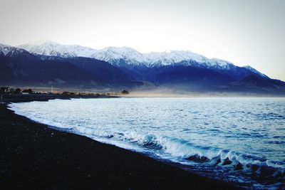 Scenic view of sea and snowcapped mountains against clear sky