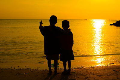 Silhouette friends on beach against sky during sunset