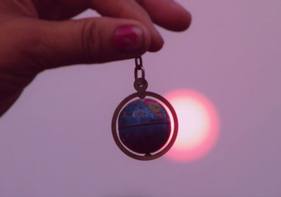 Cropped hand holding globe against sky during sunset