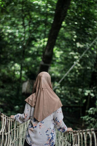 Rear view of woman standing on footbridge against trees in forest