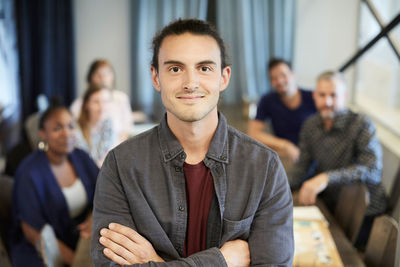 Portrait of confident businessman standing while colleagues in background at creative office