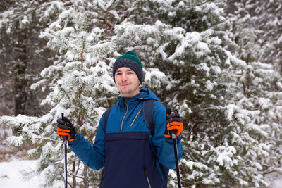 Skier with a backpack and hat with pompom with ski poles in his hands on background 