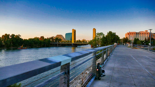 Footpath by river and buildings against clear blue sky