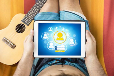 Midsection of man using digital tablet while sitting on bed by guitar at home