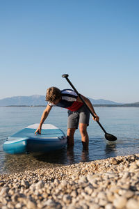 Man with paddleboard and oar standing in lake against clear sky