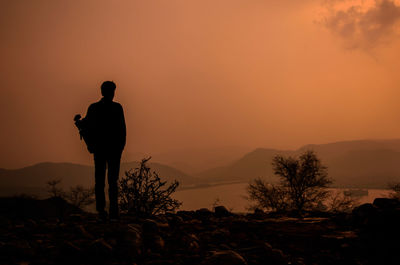 Rear view of silhouette man standing against orange sky