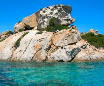 Rock formation in sea against clear blue sky