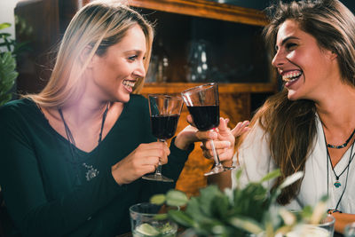 Cheerful female friends toasting wineglass at table in restaurant