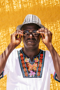 Man adjusting sunglasses while standing in front of yellow wall