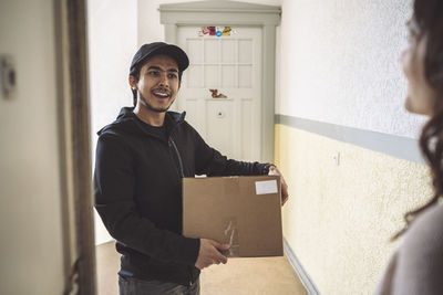 Smiling delivery man with package talking to female customer at doorstep