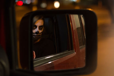 Reflection of face painted woman on side-view car mirror during halloween