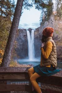 Young woman sitting on railing against waterfall