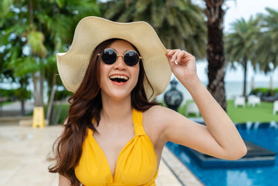 Smiling woman wearing hat standing by swimming pool