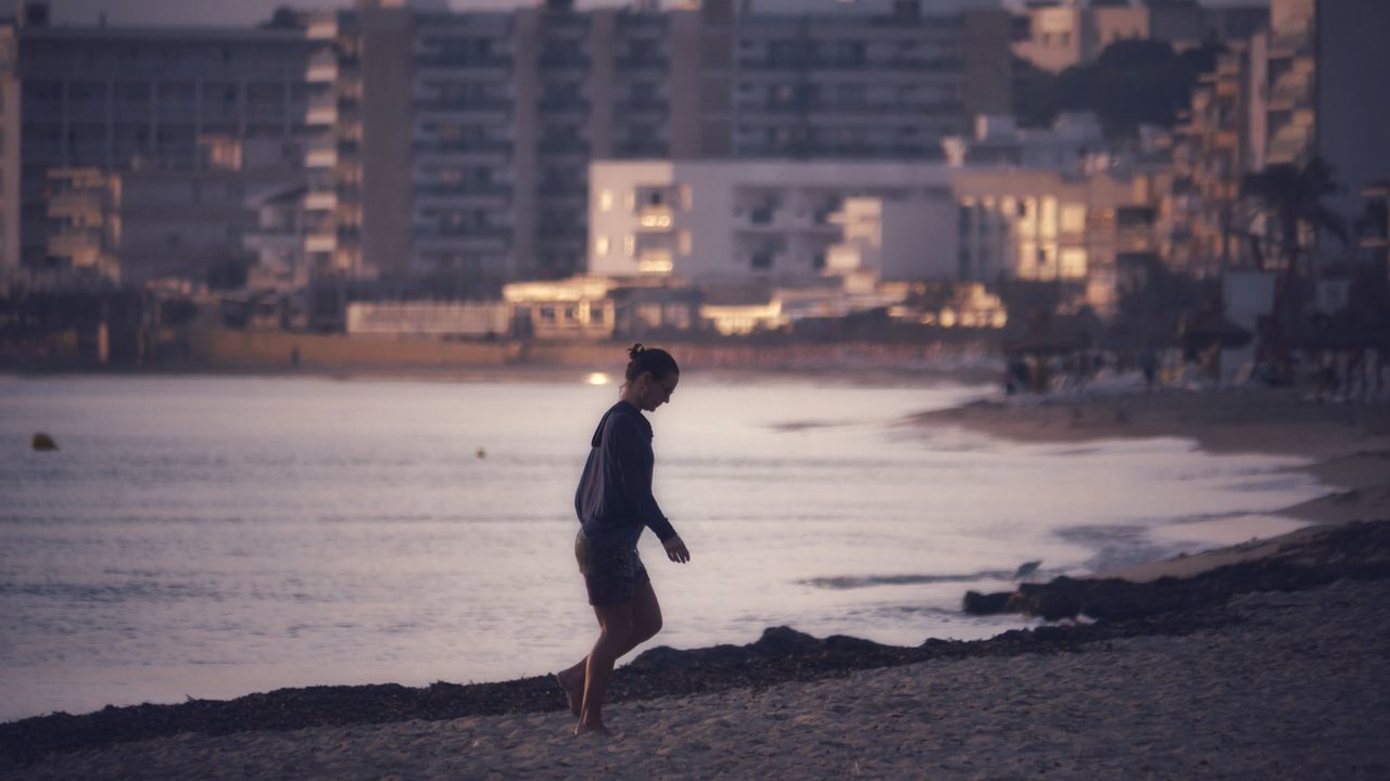 FULL LENGTH OF MAN STANDING ON BEACH AGAINST CITY