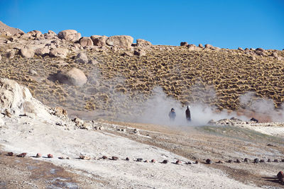 People on rocks against clear sky at tatio geysers