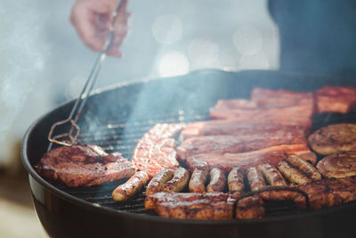 Cropped hand of person roasting meat on barbecue grill