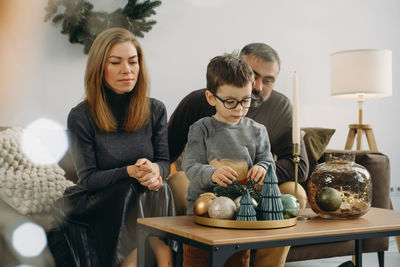 Family with child playing near christmas tree. child unpacking gifts,  parents enjoy christmas tree