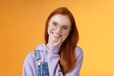 Woman in eyeglasses with hand on cheek against yellow background