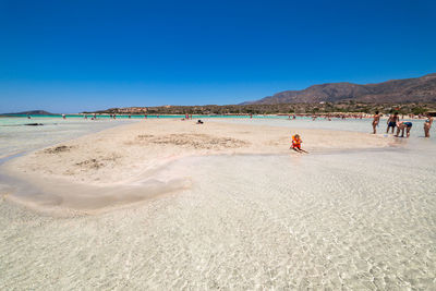 People on beach against clear blue sky