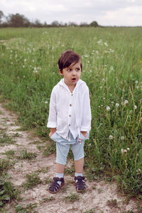 Boy child in a green field in summer in a white shirt with a hood made  linen in shorts and sandals