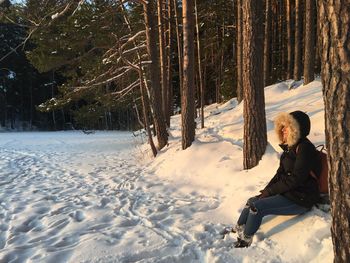 Man sitting on snow field against trees during winter