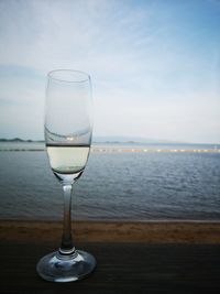 Drinking glass on table by sea against sky