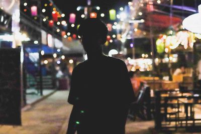 Silhouette man standing against illuminated sidewalk cafe at night