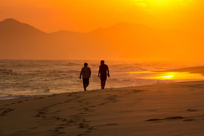 Silhouette men on beach against sky during sunset