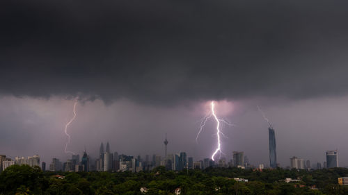 Lightning over buildings in city against sky at night