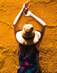 Woman with arms raised against yellow wall