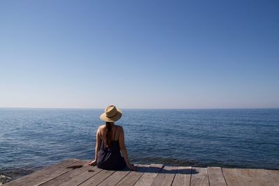 Rear view of woman sitting by sea against clear sky