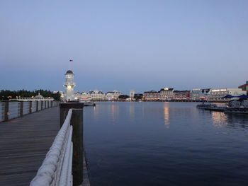 Lighthouse amidst buildings by sea against clear sky