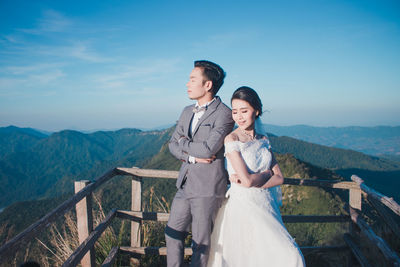 Full length of young woman standing on railing against sky