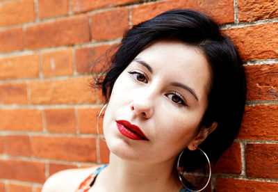 Close-up portrait of a young woman against brick wall