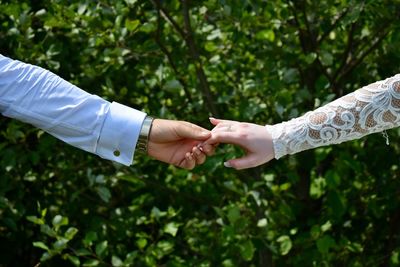 Midsection of couple holding hands against plants