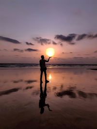 Silhouette man standing on beach against sky during sunset