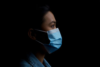 Close-up of young woman wearing flu mask standing against black background